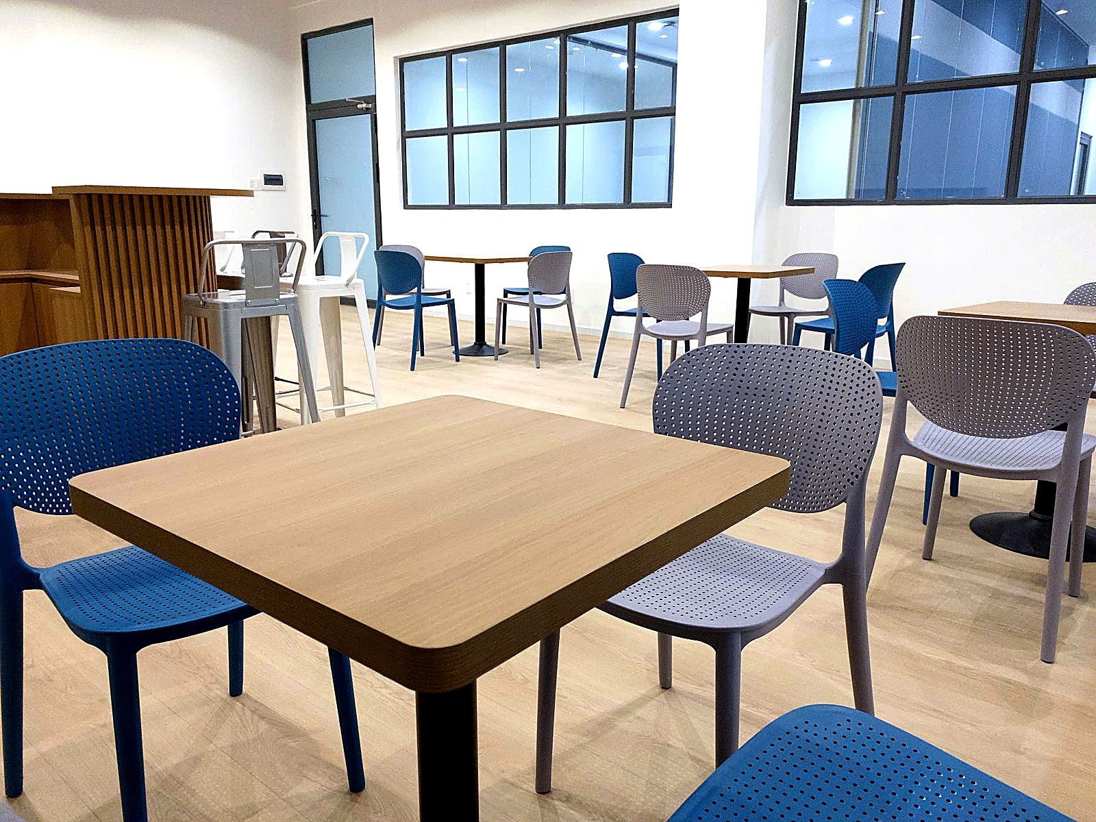 The Flexed breakout lounge with blue and grey chairs at wood tables beside tall windows.